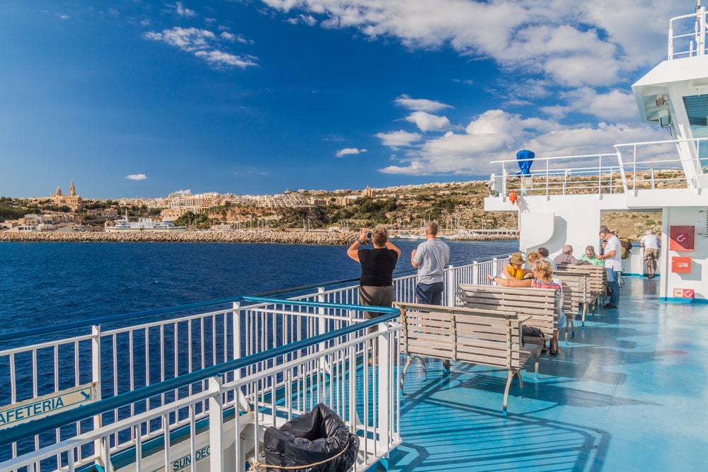  Deck of the Ferry from Mgarr on Gozo island to Cirkewwa,. Passengers on the deck of a ferry approaching a coastal town under a clear blue sky, exploring things to do in Malta.