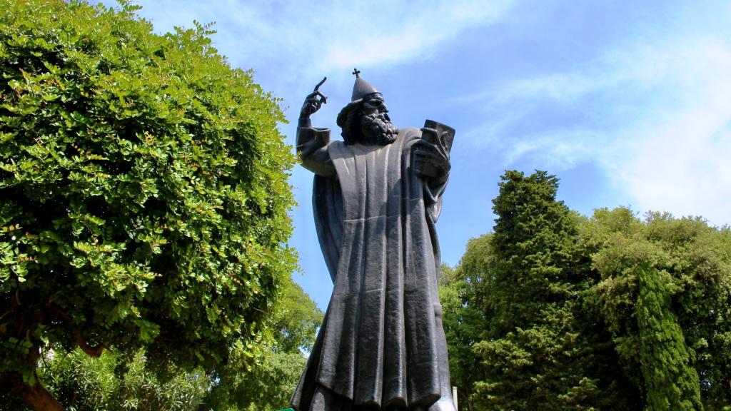 Statue of a bearded figure with a raised arm holding a sword against a blue sky, flanked by green foliage, is one of the key things to do in Split, Croatia.