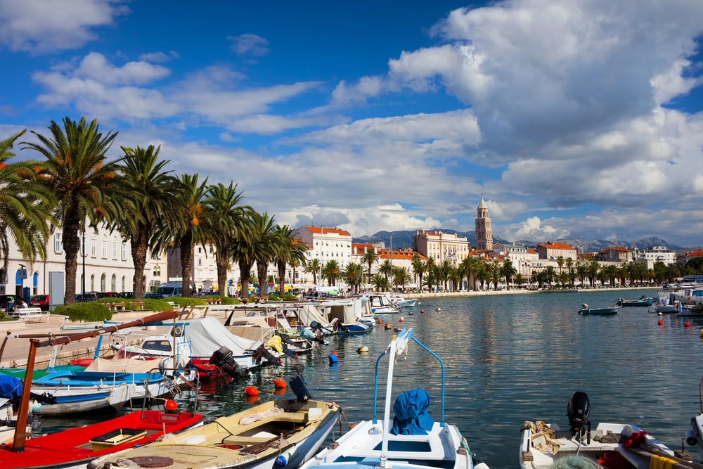 Picturesque coastal town with palm-lined promenade and moored boats under a partly cloudy sky, offering various things to do in Split Croatia.