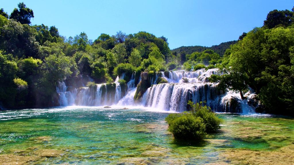 A series of picturesque waterfalls flowing into a vivid turquoise river surrounded by lush greenery on a sunny day, offering ideal things to do in Split, Croatia.