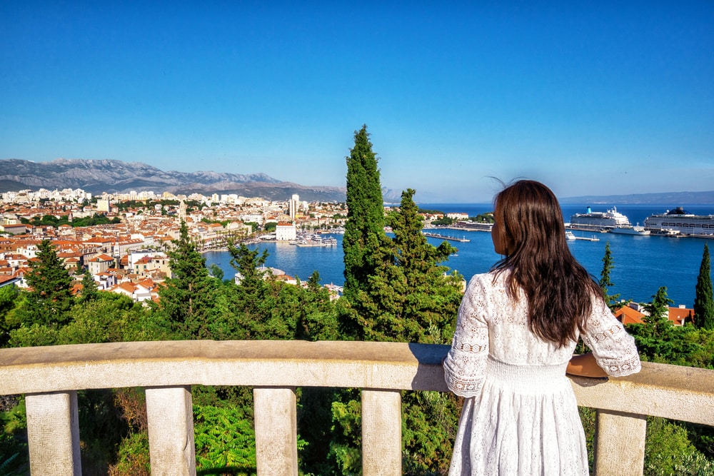 Woman overlooking a coastal cityscape from a balcony on a clear day, pondering things to do in Split, Croatia.
