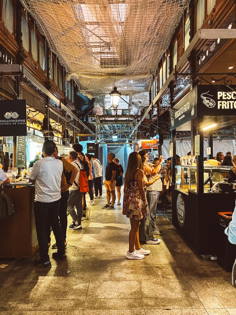 An indoor market in Madrid with bustling food stalls and people exploring various eateries.
