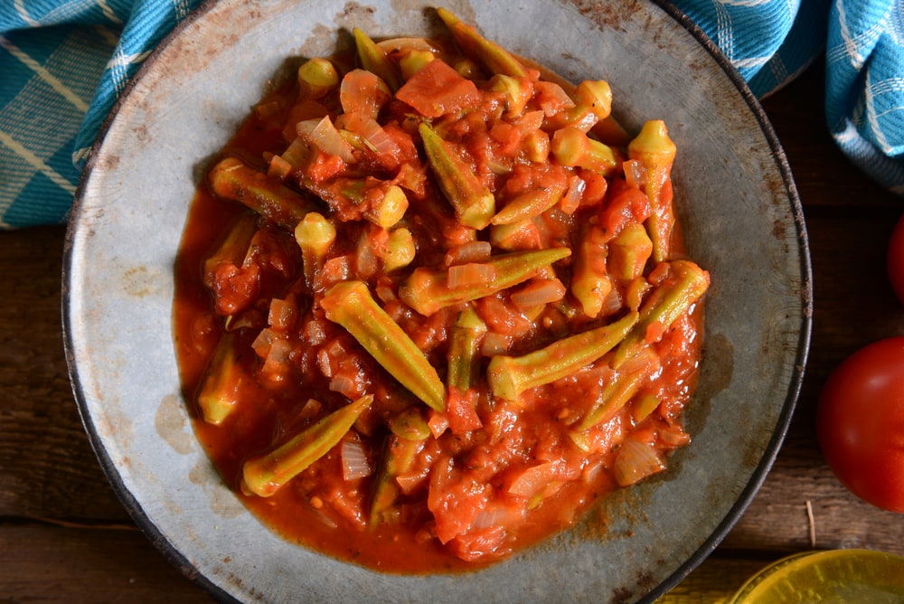 A plate of West African tomato-based vegetable stew with okra, served on a rustic wooden table.