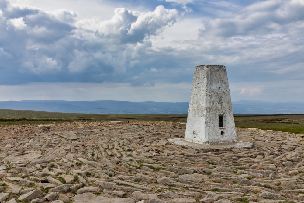 Triangulation pillar on a rocky summit with expansive views under a cloudy sky, reminiscent of the landscapes surrounding sites of the Witch Trials in England.