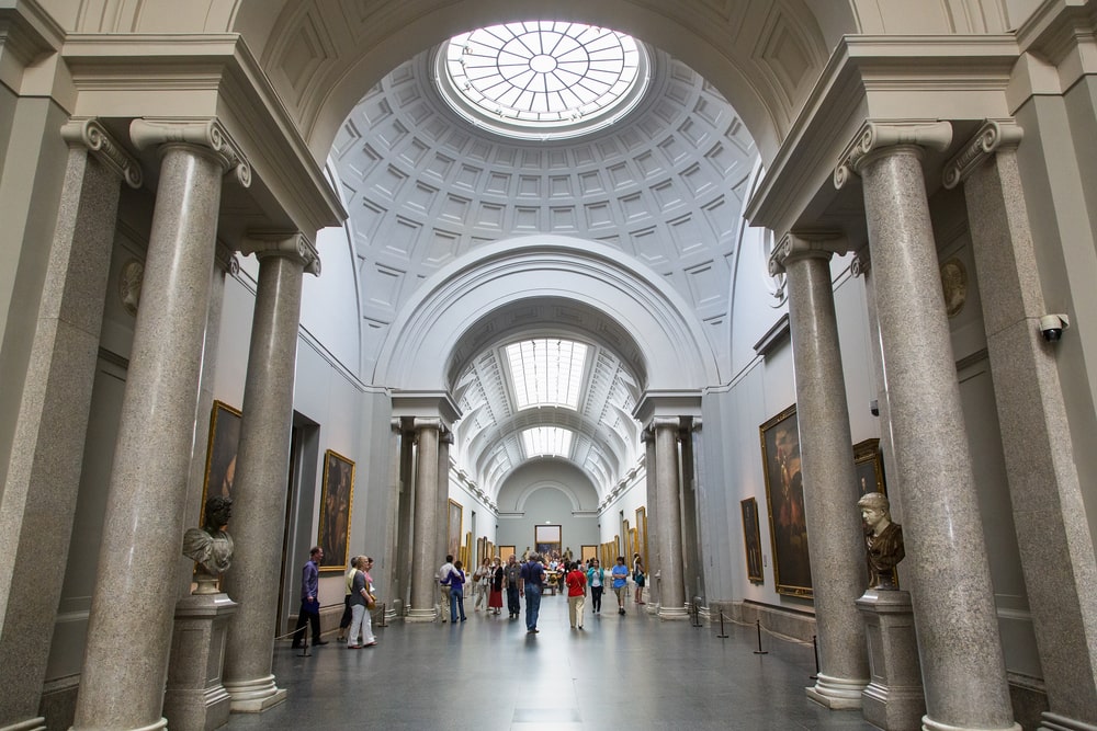 Grand hall of a museum in Madrid with visitors admiring art and architecture.