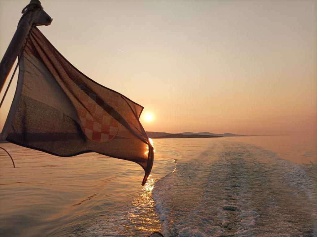 A Croatian flag flutters in the wind at sunset on a moving boat, leaving a trail on the water, showcasing one of the picturesque things to do in Split, Croatia.