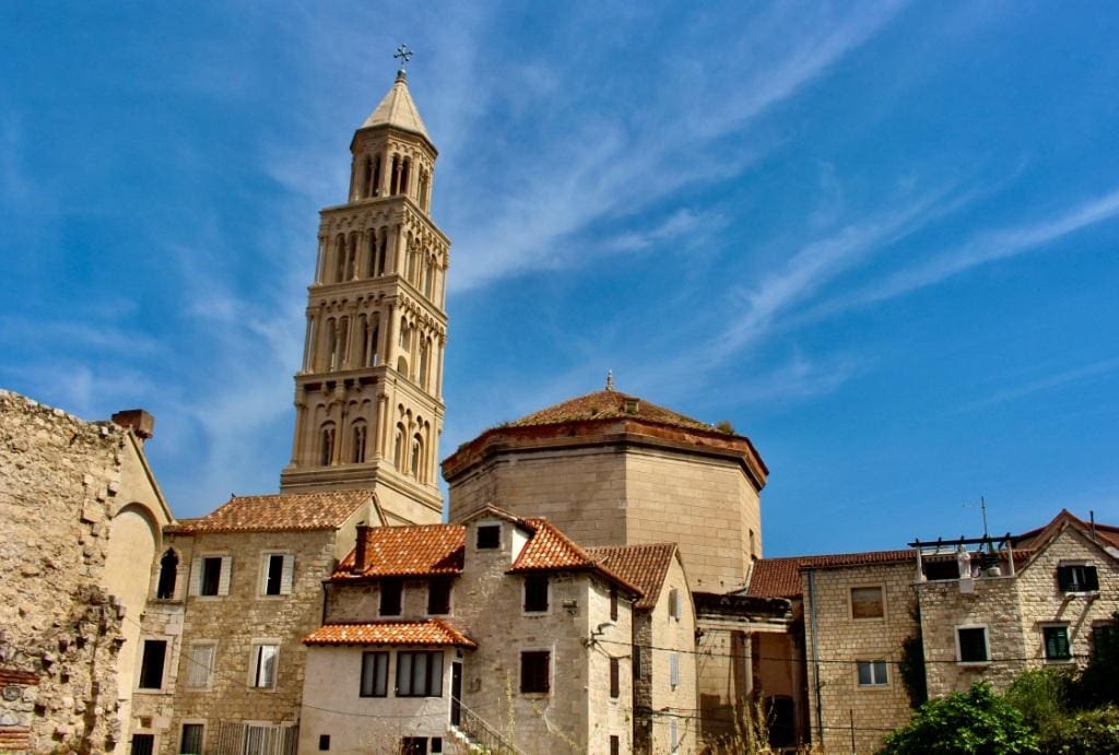 Historic stone buildings and a tall bell tower under a blue sky with scattered clouds are major attractions among the things to do in Split Croatia.