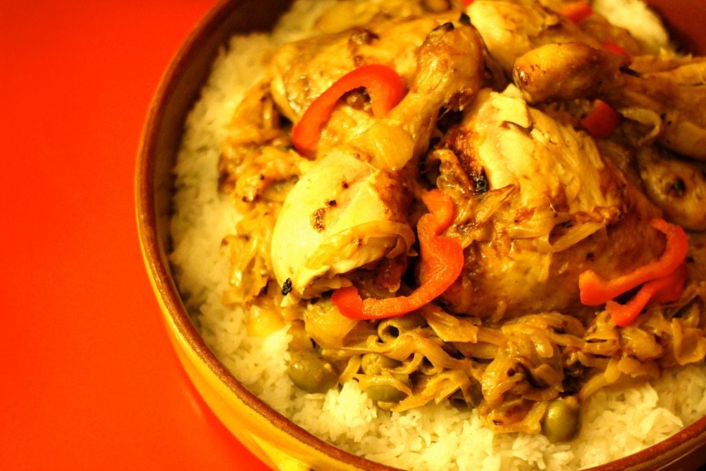 A bowl of West African food: rice topped with cooked chicken and red pepper slices.
