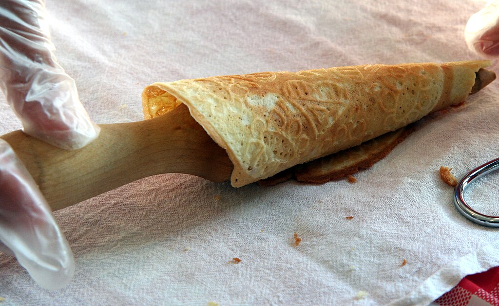 A person is cutting a Norwegian krumkake with a knife.