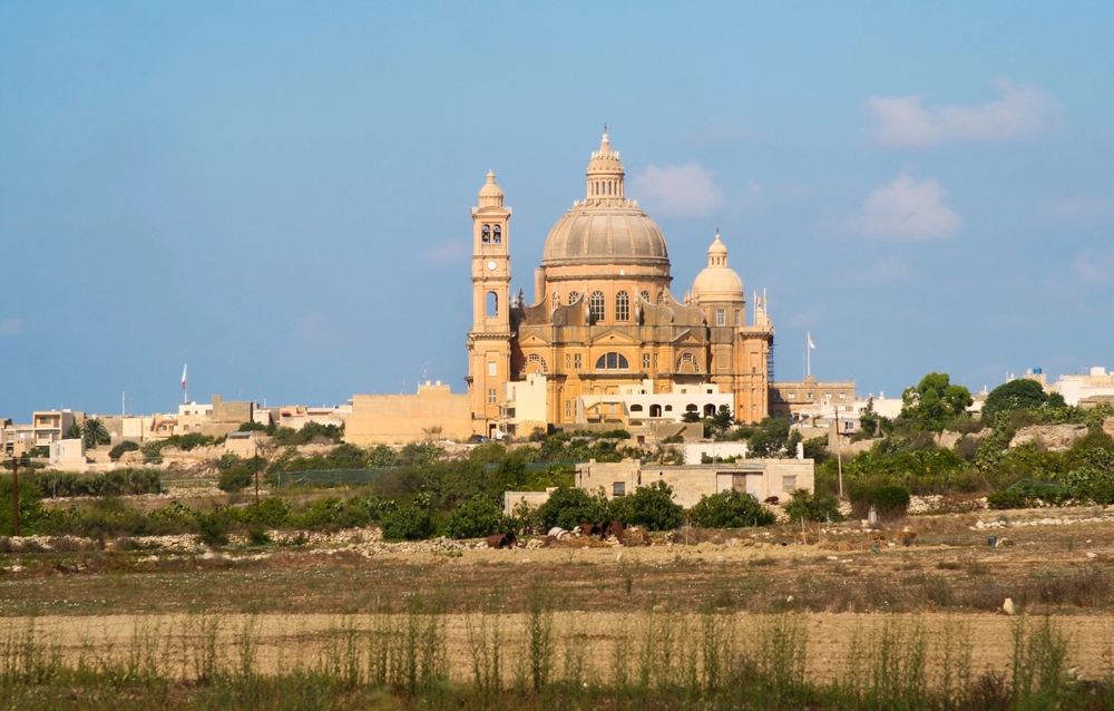 A historic church with twin bell towers, a popular attraction among things to do in Malta, rises above surrounding buildings in a rural landscape.