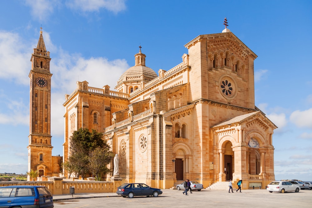 Stately sandstone church with a tall belfry under clear blue skies, a must-see for things to do in Malta. Ta' Pinu Church in village Gharb, Gozo island, Malta. The famous Madonna church is dedicated to the Blessed Virgin of Ta' Pinu.