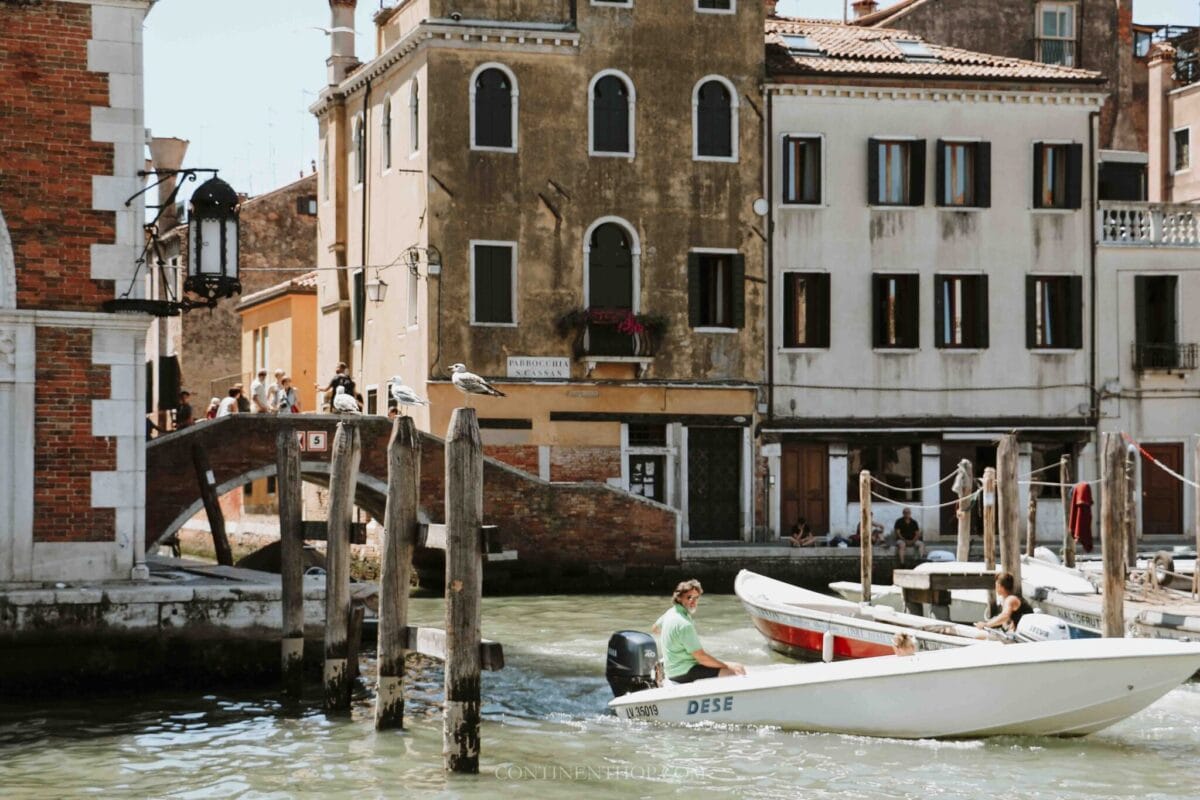 A man in a boat on water with buildings and a boat, showcasing one of the best places to visit in Italy.