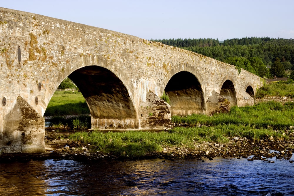 Stone bridge with multiple arches over a river with grassy banks under a clear sky, showcasing stunning views and things to do in Tipperary.