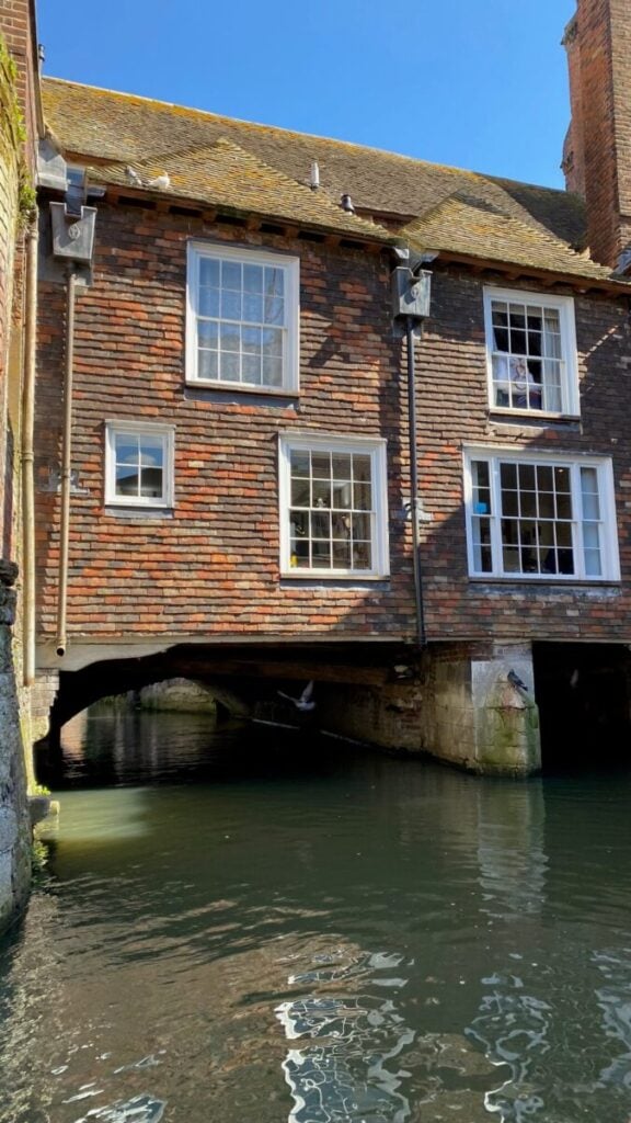 A historic brick building with arches over a canal, reflecting on the water's surface, perfect for Canterbury boat trips.