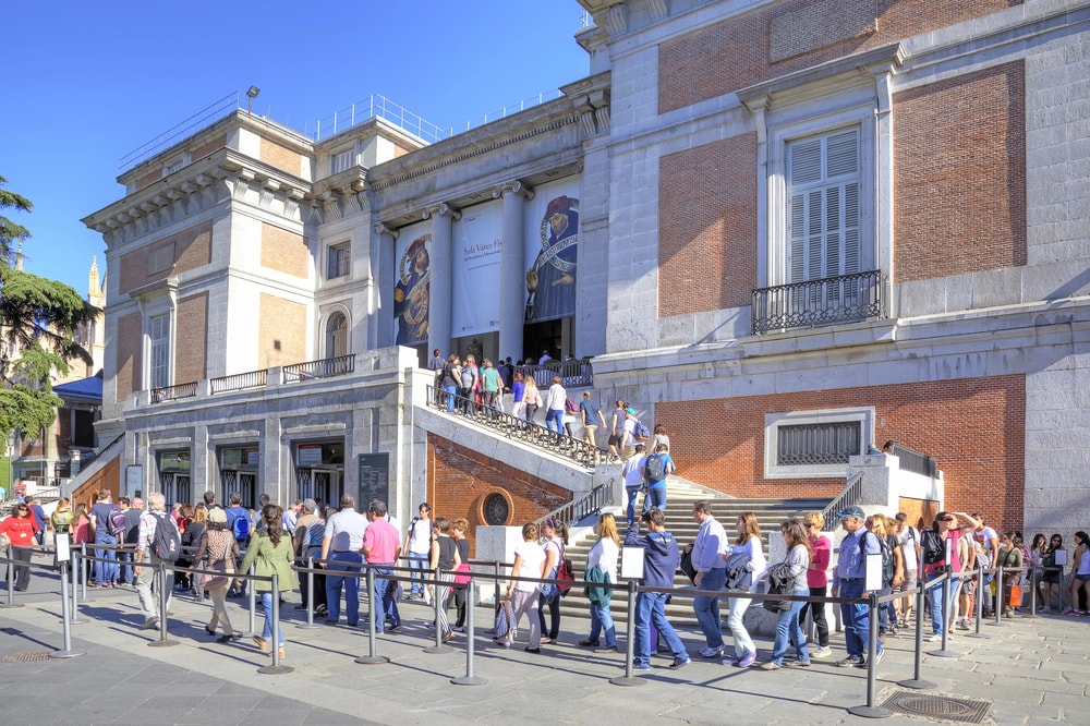 Visitors queuing outside a museum on a sunny day in Madrid.