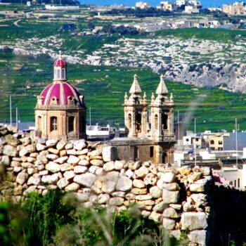 Historic church with a distinctive dome and twin bell towers, viewed from beyond a stone wall in a lush landscape, is one of the things to do in Malta.