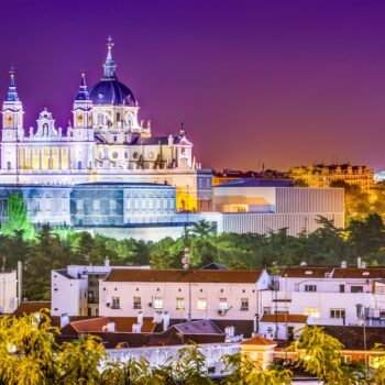 Twilight skyline of Madrid featuring the Royal Palace and Almudena Cathedral with illuminated domes during one day in Madrid.