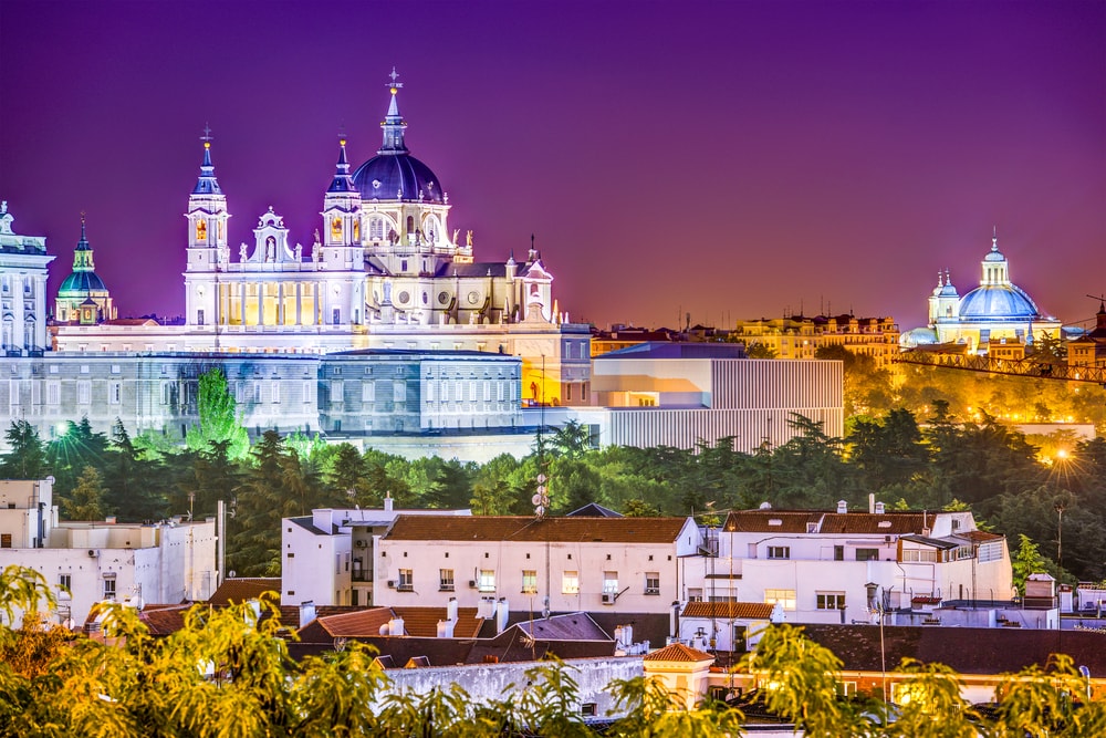 Twilight skyline of Madrid featuring the Royal Palace and Almudena Cathedral with illuminated domes during one day in Madrid.