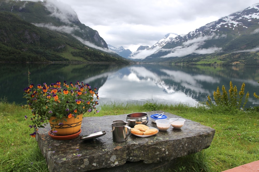 Breakfast with a view in Norway - cloudy Nordfjord view in Olden. A stone table in front of a lake, showcasing food in Norway.