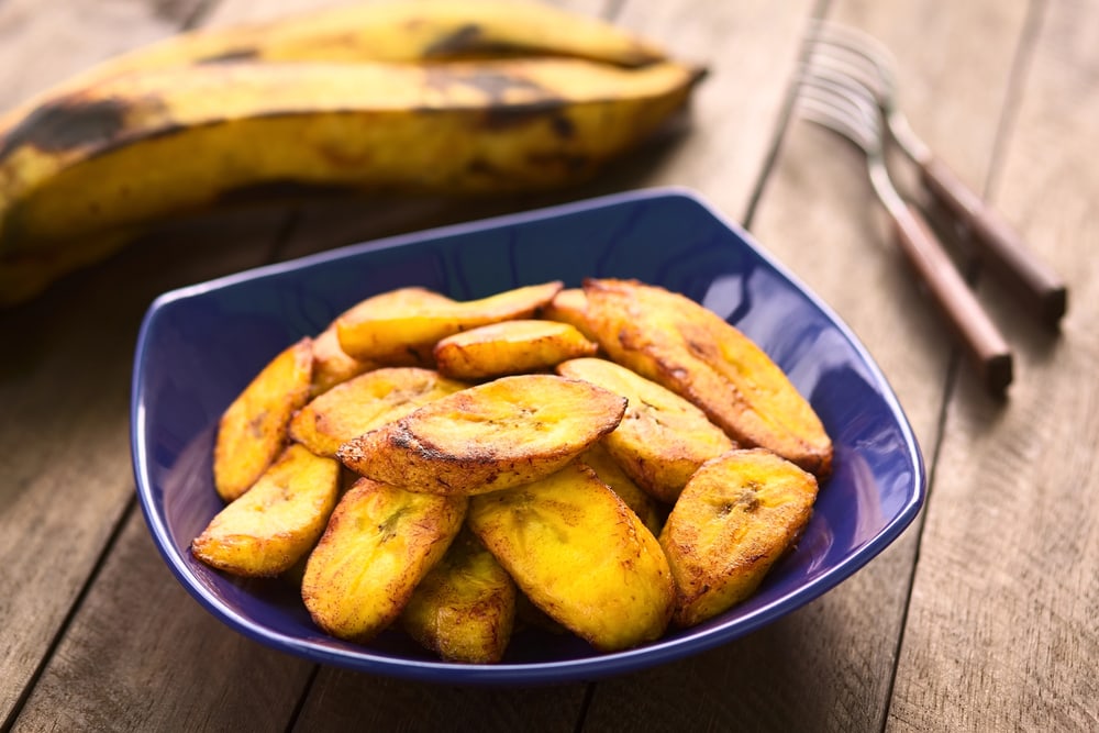 West African food: Fried plantains served in a blue bowl with whole plantains and a fork in the background.