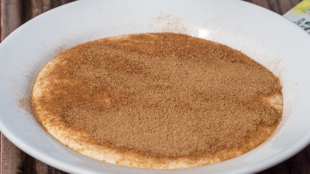 A bowl with cinnamon in it on a table, symbolizing a typical spice used in food in Norway.'Rømmegrøt' is Norwegian porridge made with sour cream, whole milk, wheat flour, butter, and salt. it is thick and sweet and is generally drizzled in butter and sprinkled with sugar and ground cinnamon