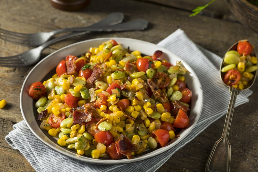 A bowl of succotash, one of the national dishes, with corn, lima beans, tomatoes, and bacon on a rustic table.