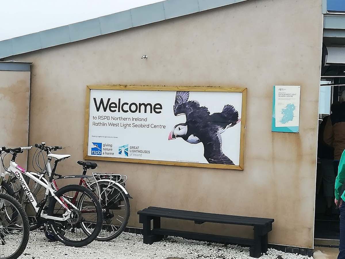 Welcome sign for Rathlin West Light Seabird Centre in Northern Ireland with a puffin illustration and bicycles.