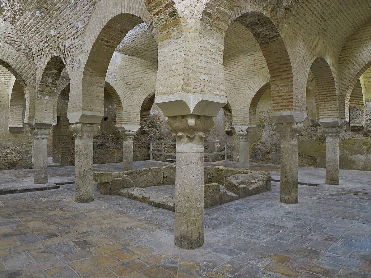 A stone room features multiple arched brick ceilings supported by columns surrounding a central stone basin.