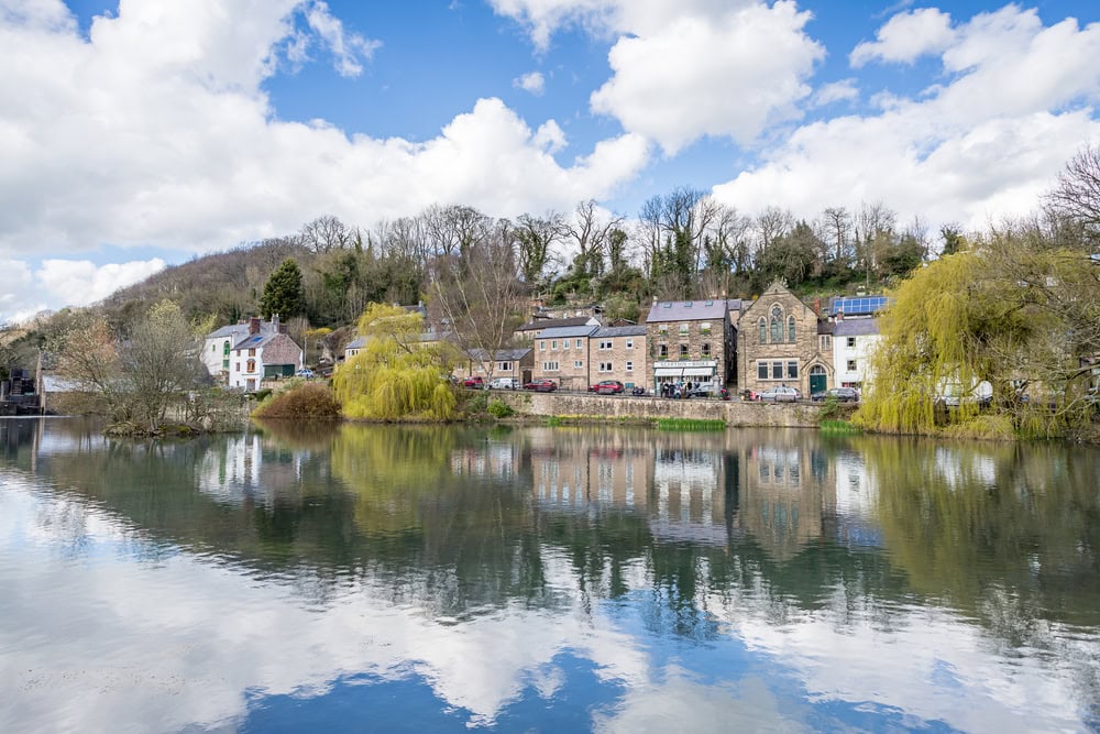 Cromford Mill Pond pictured on a bright spring day in March 2024 surrounded by willow trees and old houses.