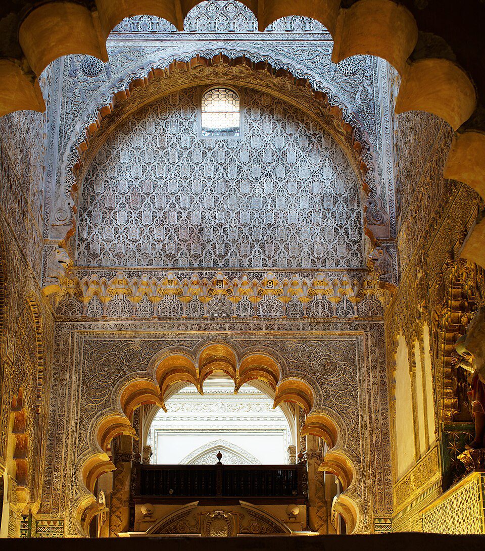 Intricate carved stone arches and walls feature detailed geometric patterns and a small window in a high-ceilinged interior.