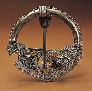 An ornate, circular silver brooch features intricate metalwork, a central pin, and decorative filigree patterns.