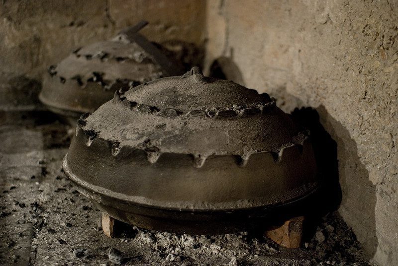 Cooking traditional balkan turkish bosnian dalmatian meal Peka in metal pots called sac sach or sache. Detail of squid or octopus with potatoes under Sache. Sac is covered with hot charcoal.