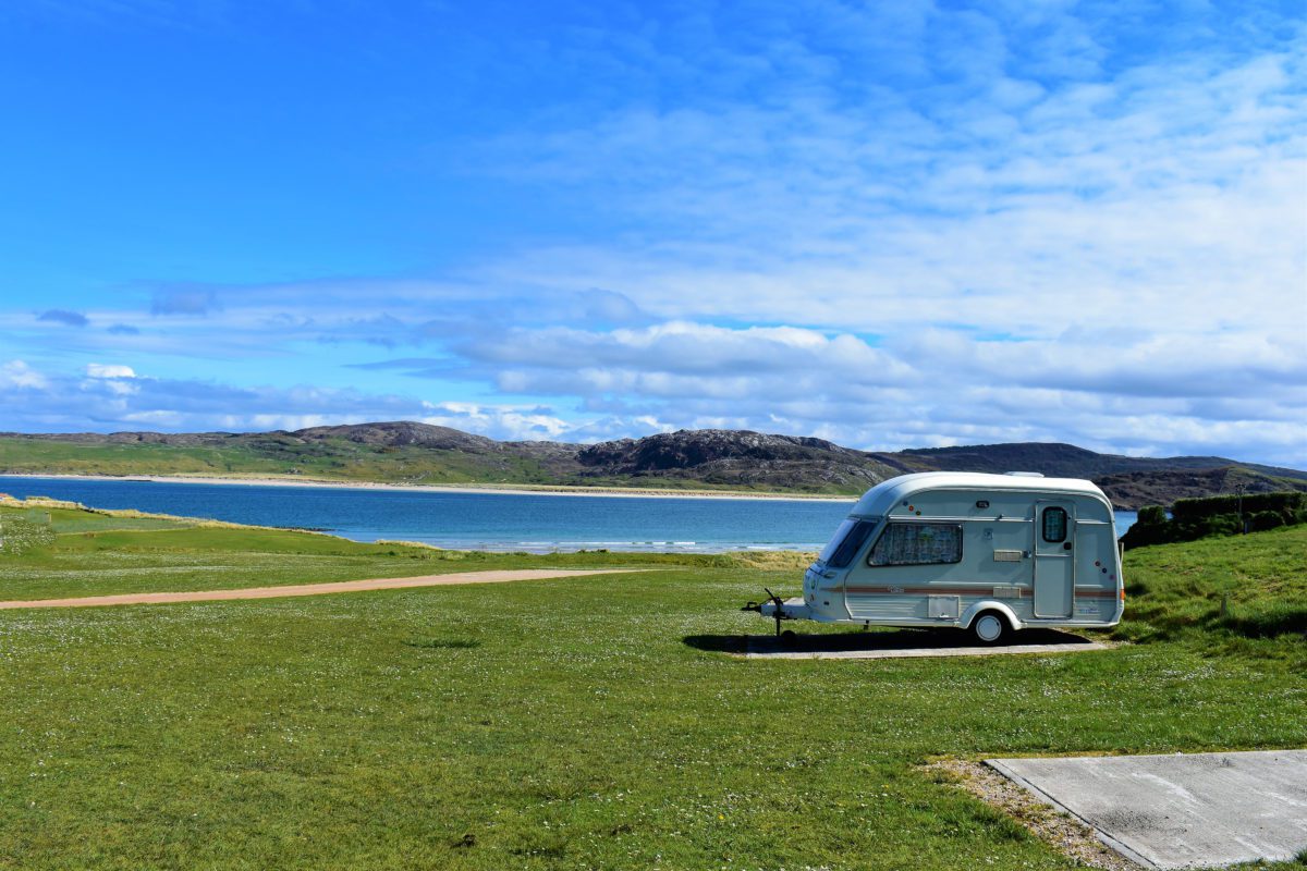 A caravan overlooks a beautiful blue bay and rugged hills on the Scottish coast.