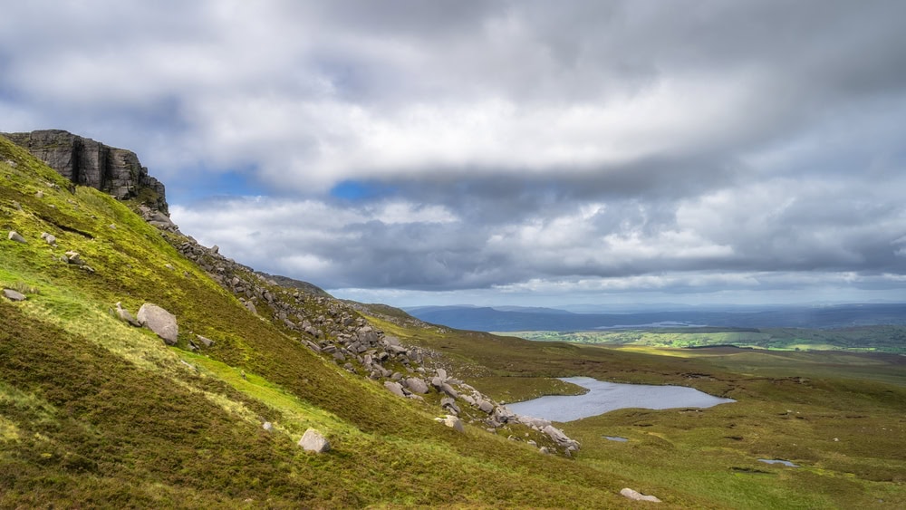 Cuilcagh Mountain Park with view on cliff, rock slide and rumble leading down to small lake surrounded by bog and wetlands Fermanagh, Northern Ireland