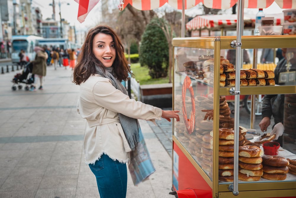 Beautiful young girl in fashionable clothes shows stall of traditional Turkish street food simit or bagel in English at Istanbul,Turkey
