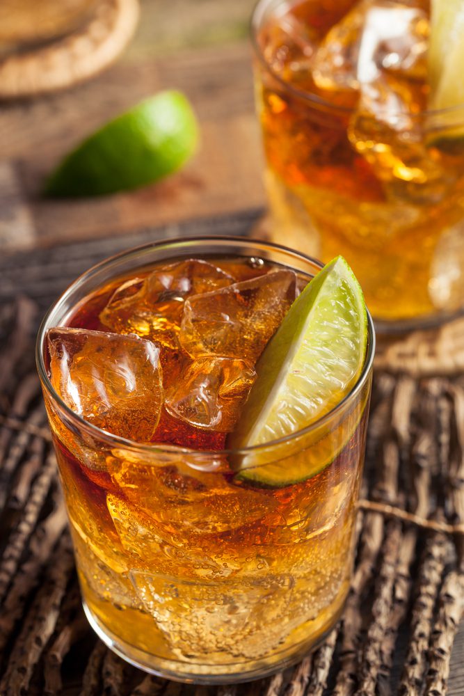 Two glasses of amber-colored iced drinks garnished with lime wedges sit on a textured surface.