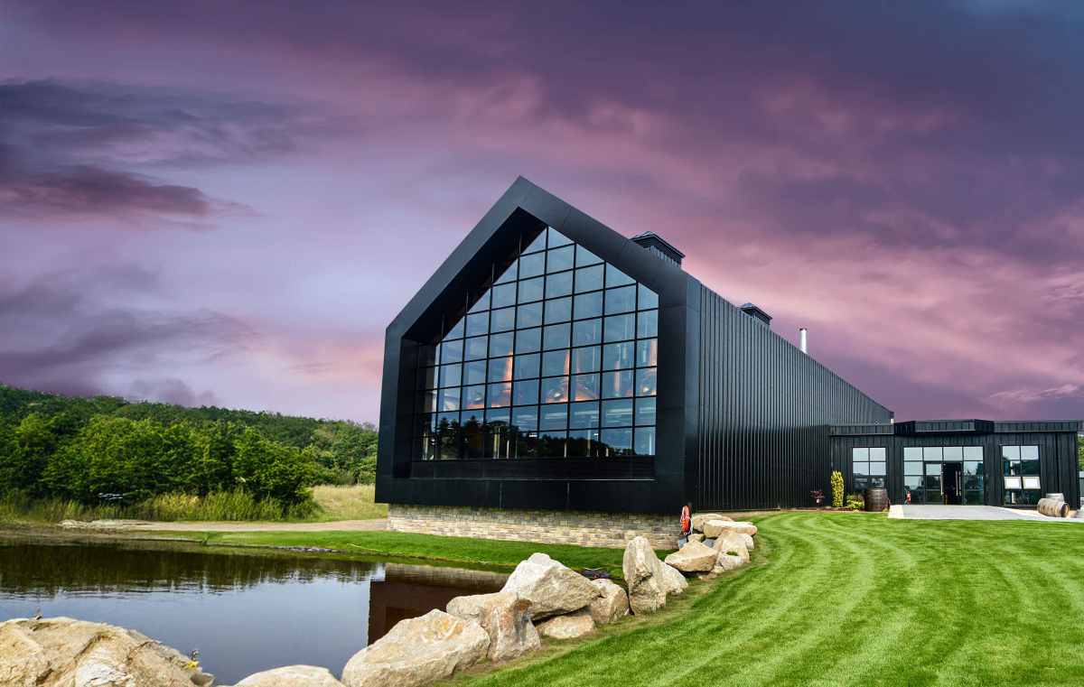 A modern black building with a large glass facade stands beside a pond and a grassy lawn under a purple sunset sky.