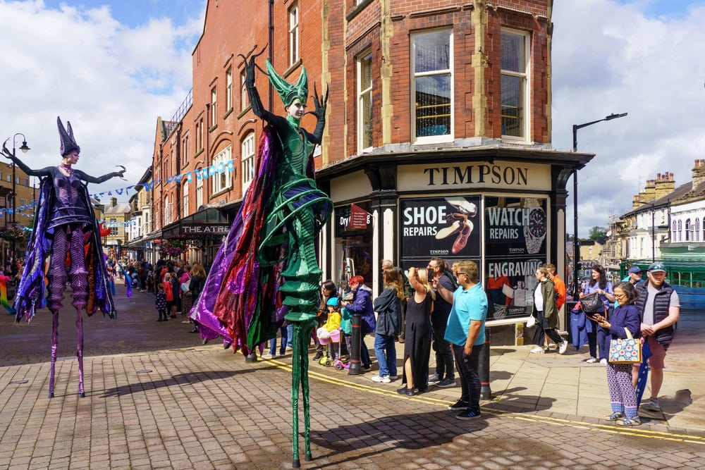 The Carnival Parade in Harrogate, featuring two female Stilt Dancers in green and purple costumes with long cloaks marching through the town centre, North Yorkshire, England, UK. Things to do in Knaresborough