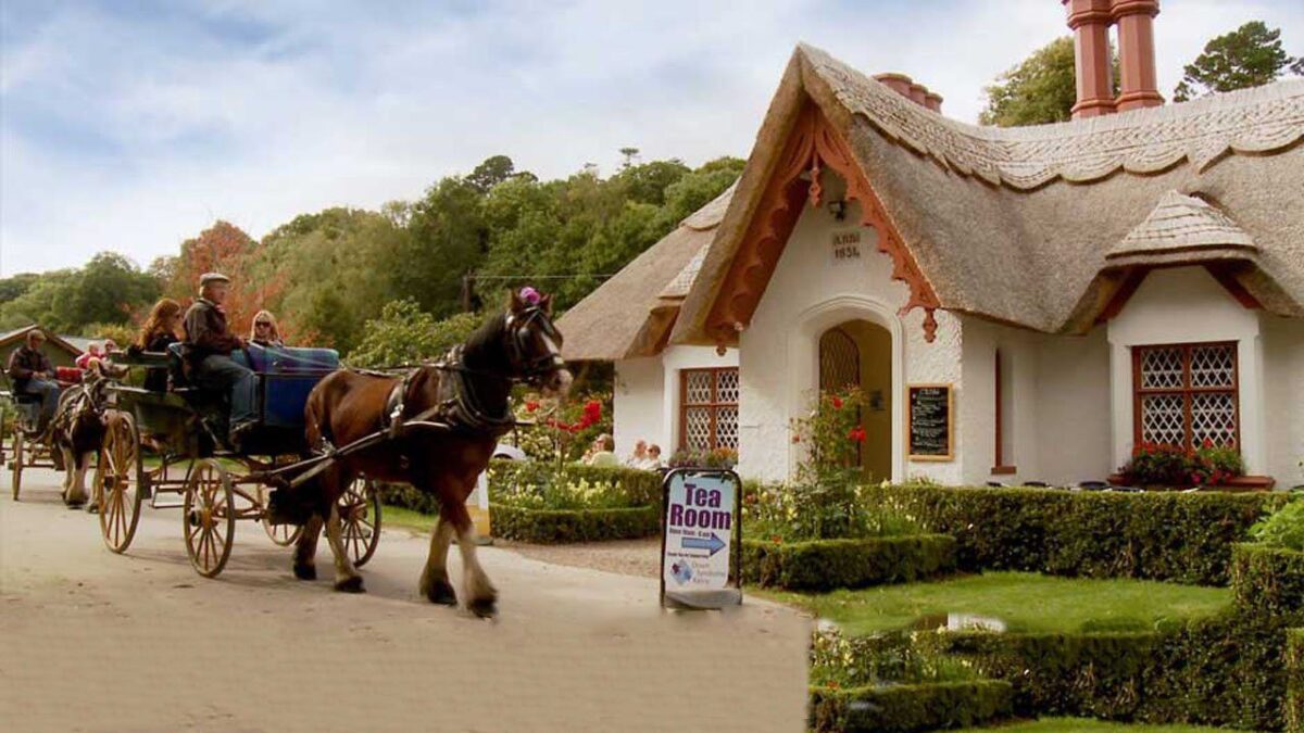 killarney horse cart takng tourists past a thatched Irish cottage