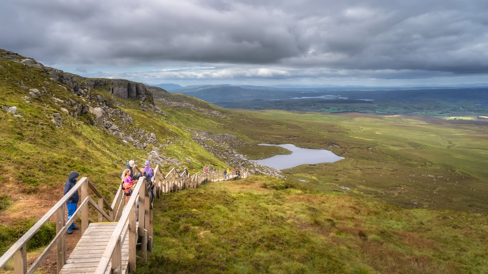 Cuilcagh Mountain Park, Northern Ireland, Auguast 2020 Group of tourists hiking on wooden boardwalk with long stairs going uphill in scenic mountains