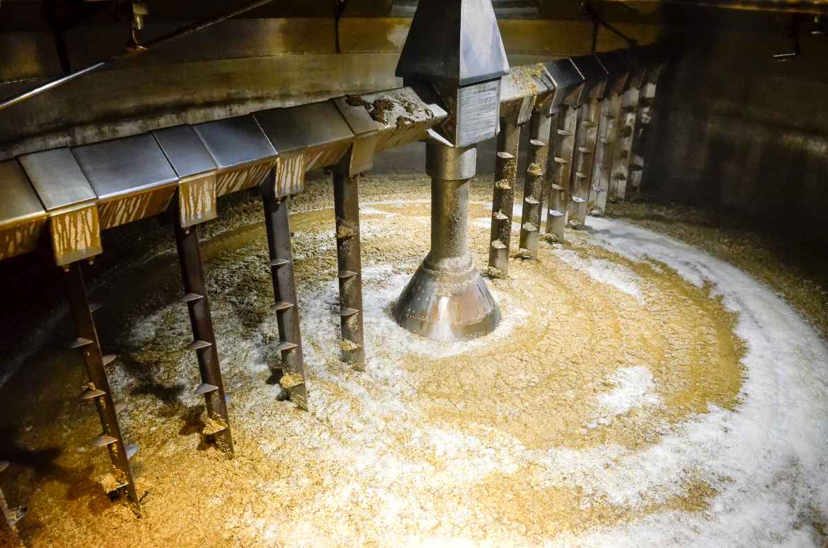 A large industrial mixer with rotating metal paddles stirs a thick, golden-brown mixture inside a circular vat.