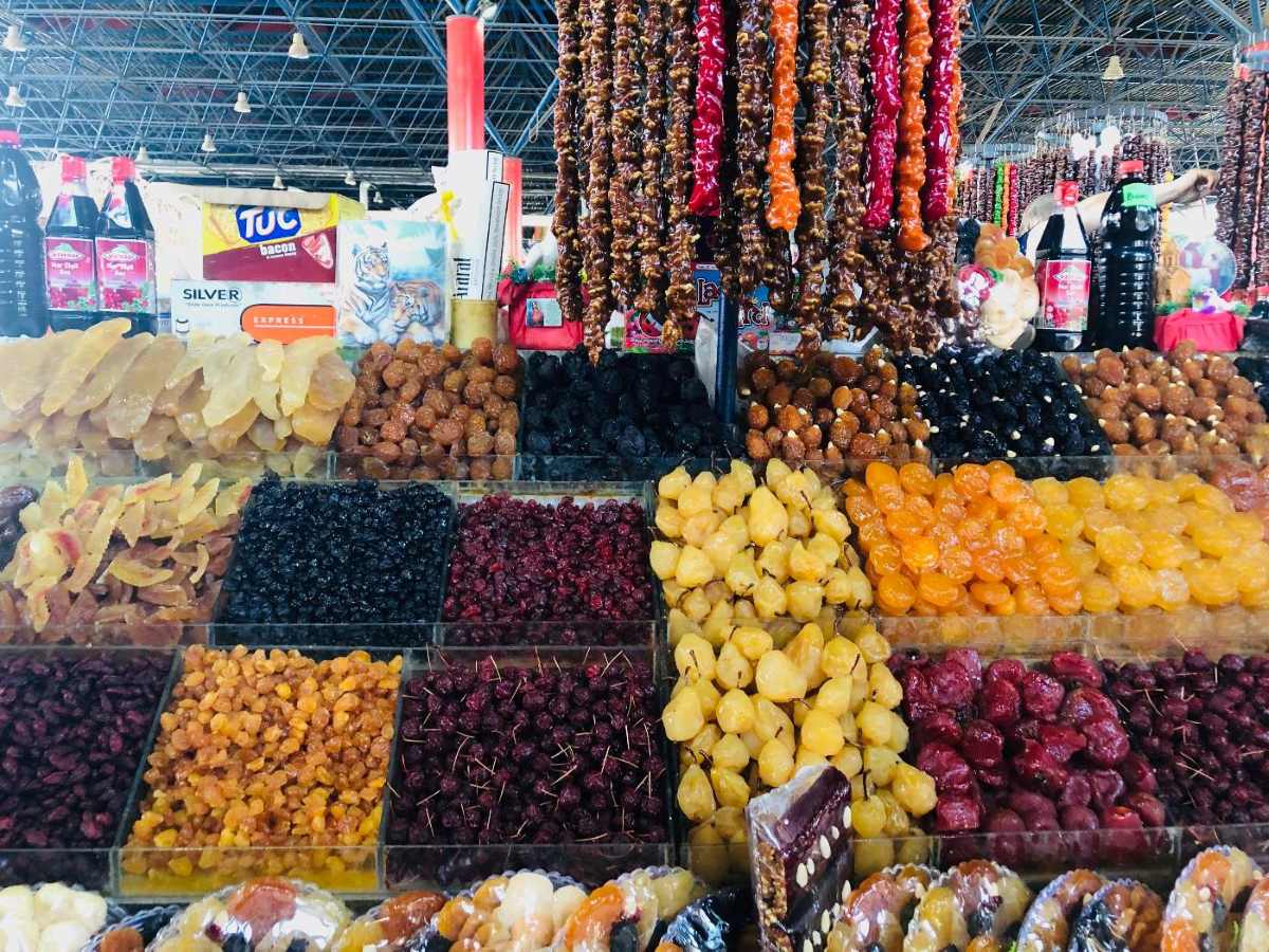 A market stall displays a variety of dried fruits, nuts, and strings of churchkhela hanging from the ceiling.