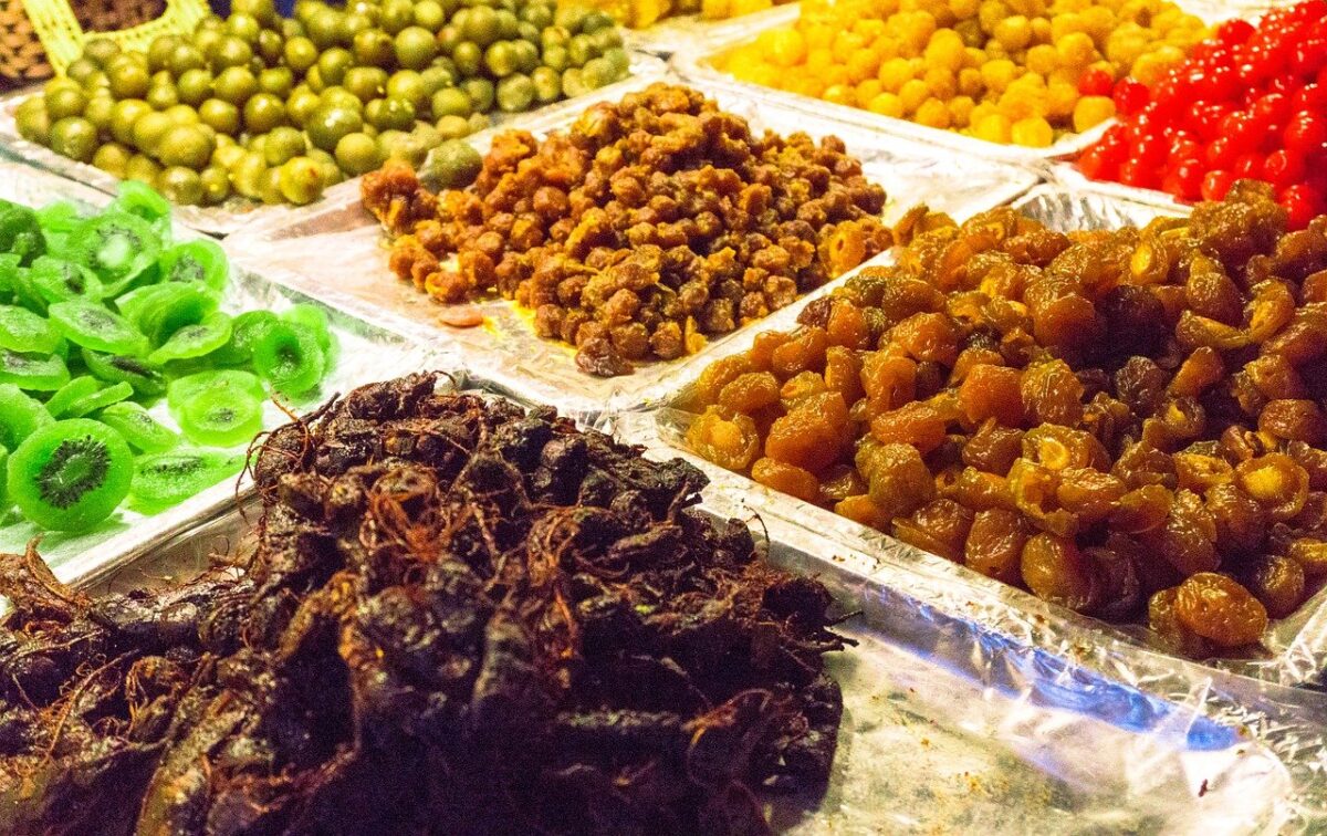 Trays of various colorful dried fruits and preserved snacks are displayed on a market stall.