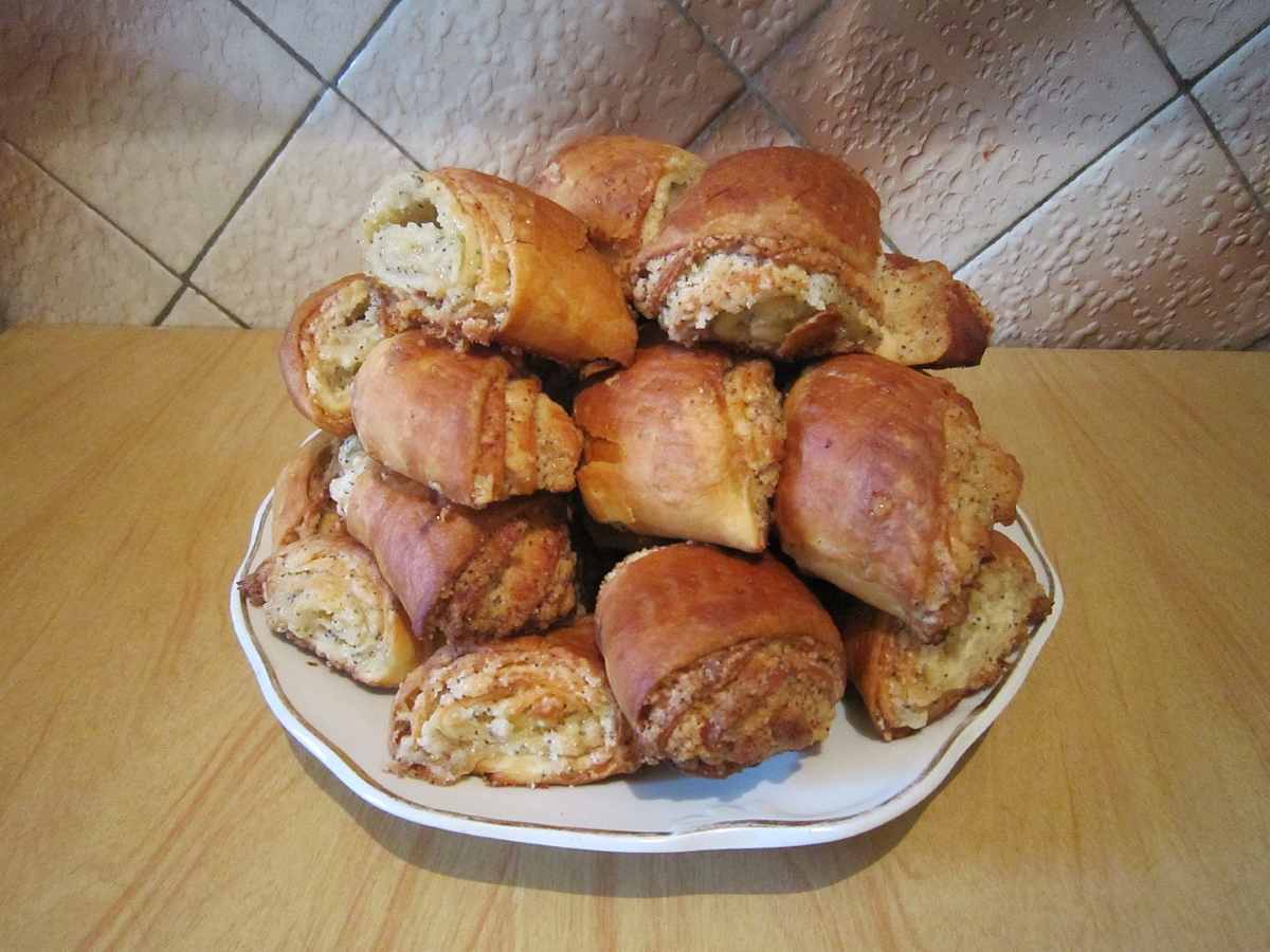 A plate piled high with golden-brown, rolled pastries sits on a wooden surface in front of a tiled wall.