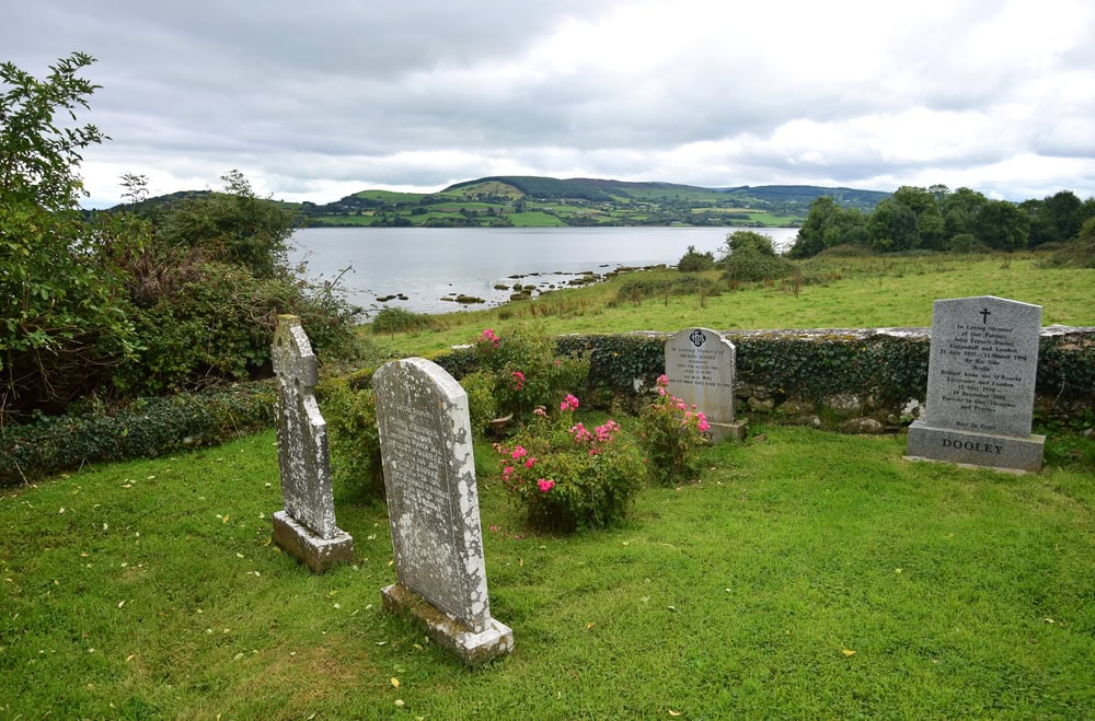 Tombstones with inscriptions on cemetery on Holy Island in Lough Derg in Ireland, County Clare. In the back Lough Derg.