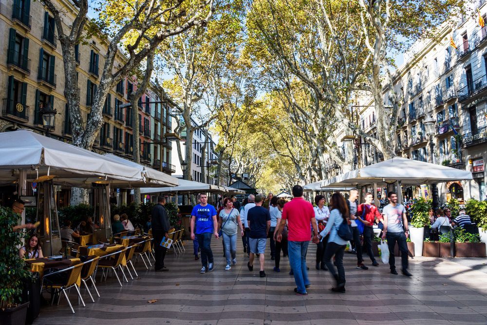 Las Ramblas barcelona a pedestrian walk through in central Barcelona. Tourists and locals walk down a tree lined avenue with cafes on either side of the avenue shaded by trees overhead