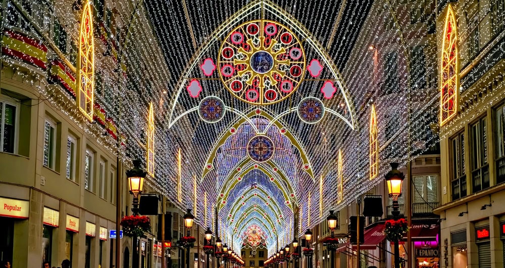 Christmas lights in Malaga arching over a narrow street of shops