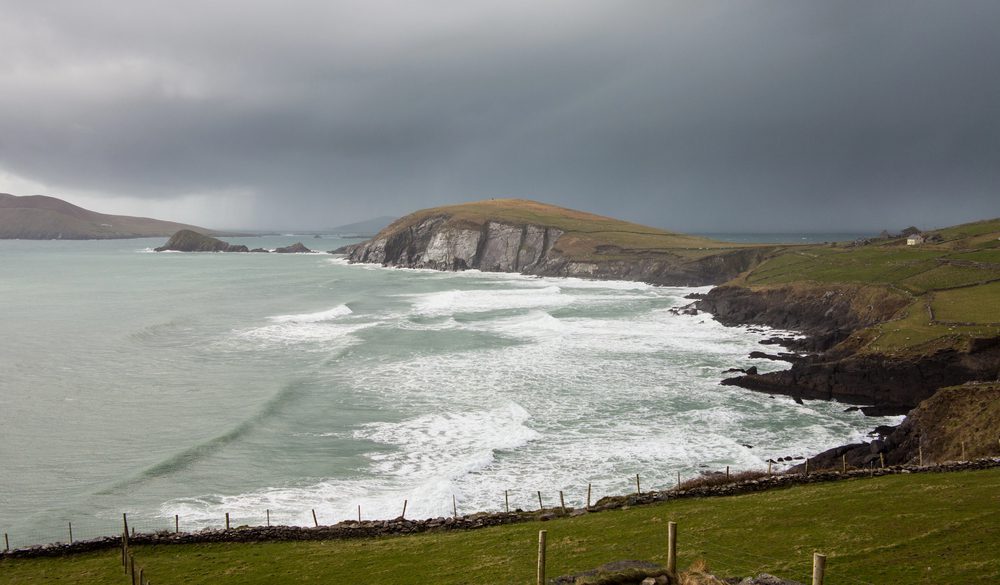 Waves crash against a rocky coastline under a dark, overcast sky.