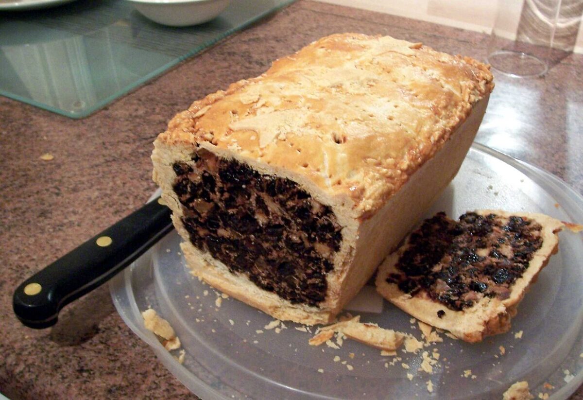 A loaf of fruit bread with a pastry crust sits on a plastic plate next to a knife.