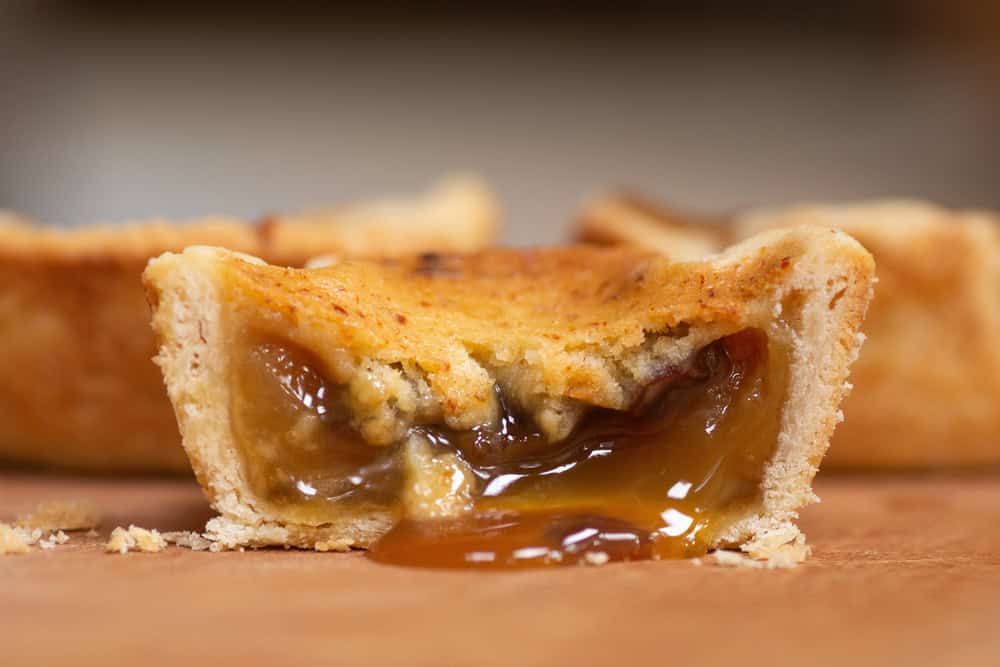 A butter tart sits on a platter, it is cut in half and the filling is oozing out in a sweet sticky stream